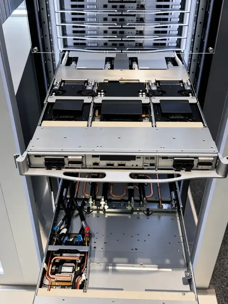 Open liquid-cooled AI server rack with stainless framing, server trays, and copper coolant lines.
