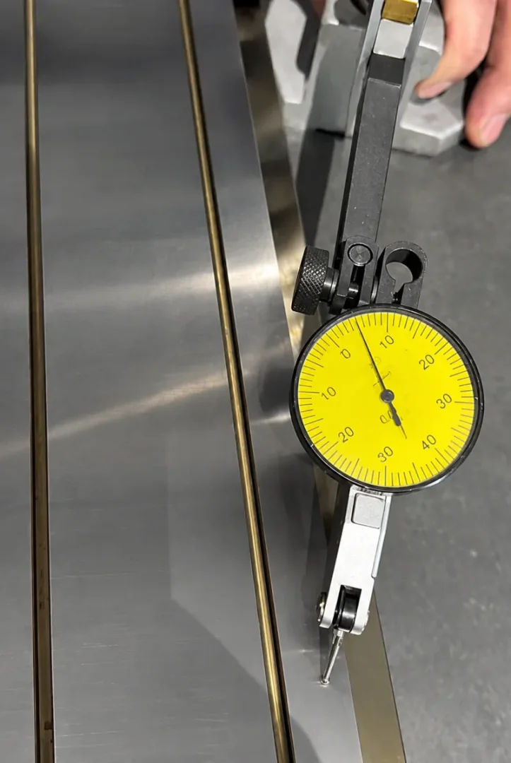 Dial indicator checking a machined stainless steel manifold sealing face for flatness.